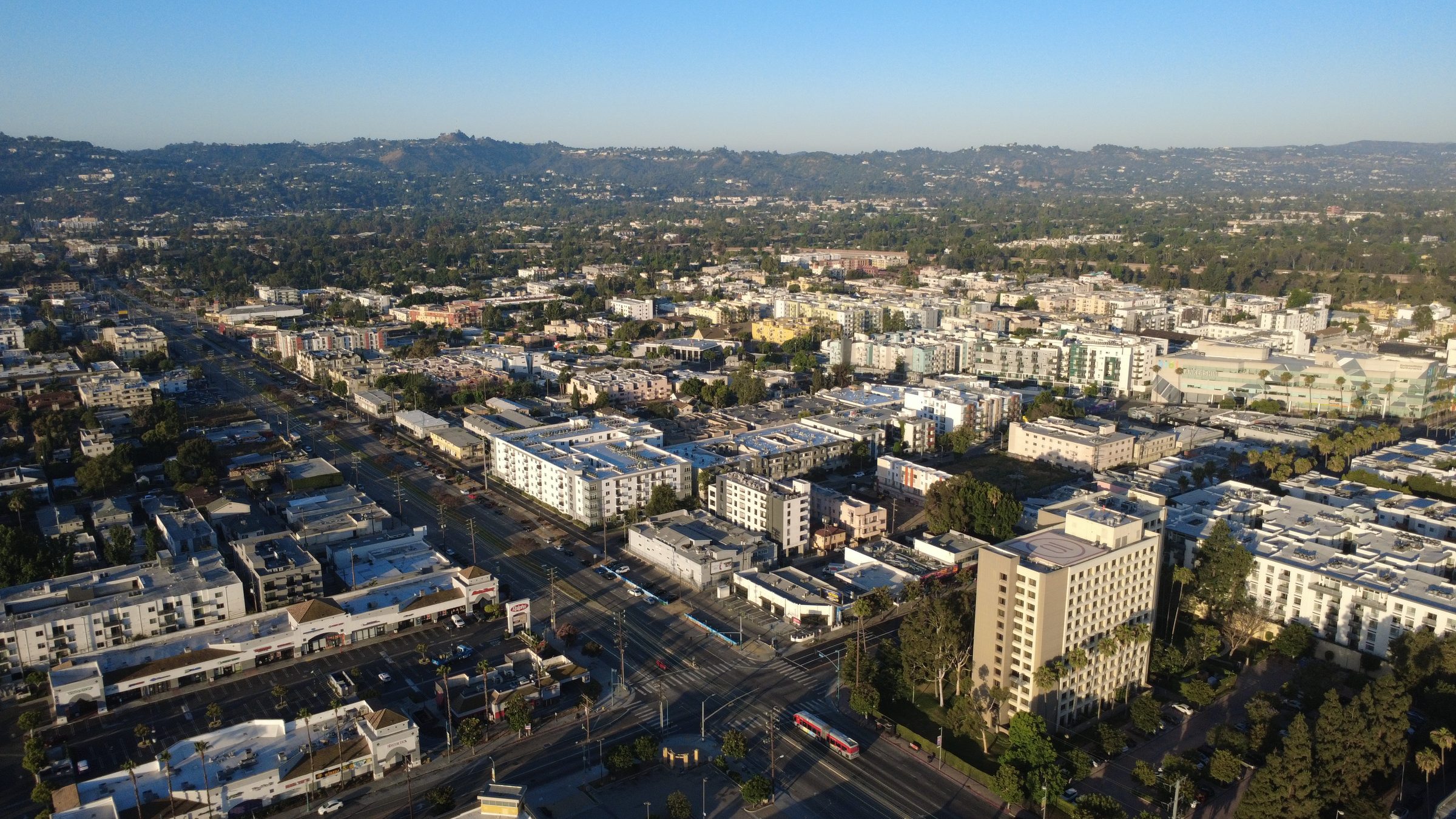 Aerial view of a Los Angeles County apartment building neighborhood, apartment buildings, tree-lined streets, and the Santa Monica Mountains in the distance.