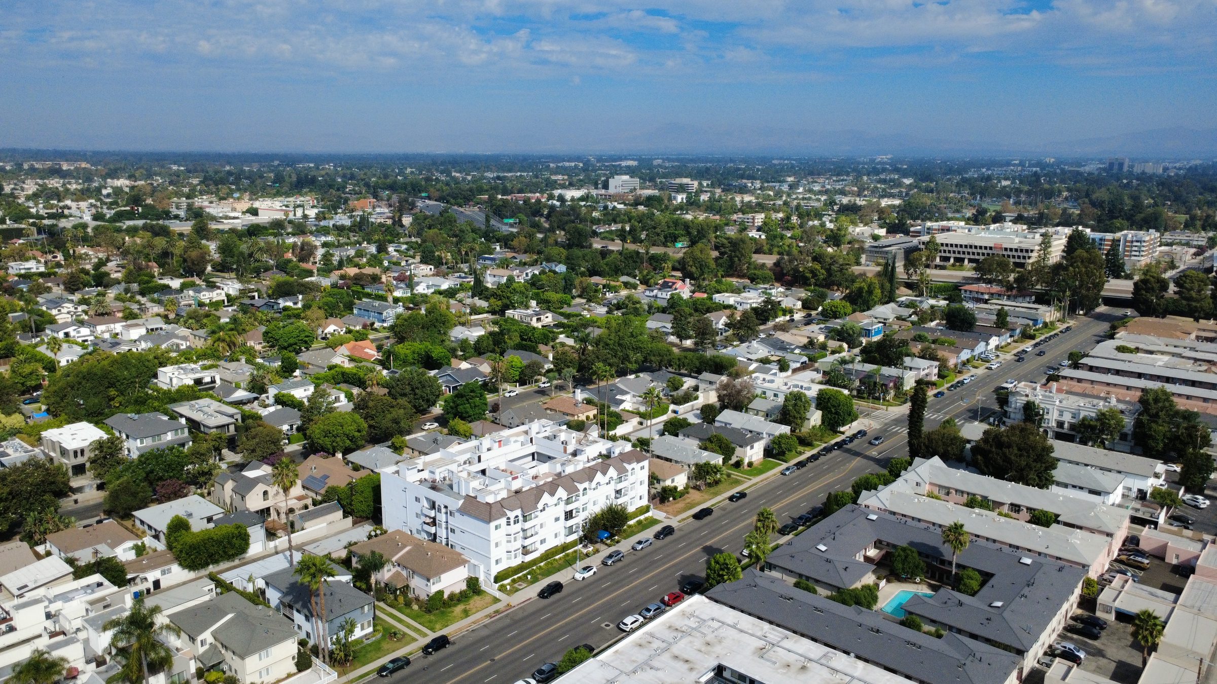 Wide aerial view of a Los Angeles County residential neighborhood, multifamily apartment buildings, main streets, and city grid stretching to the horizon.